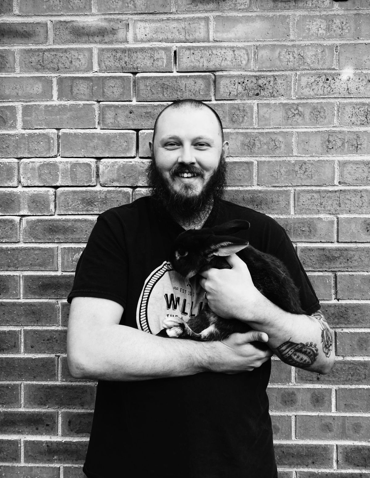 Ethan in front of a brick wall, holding a black rabbit, black and white